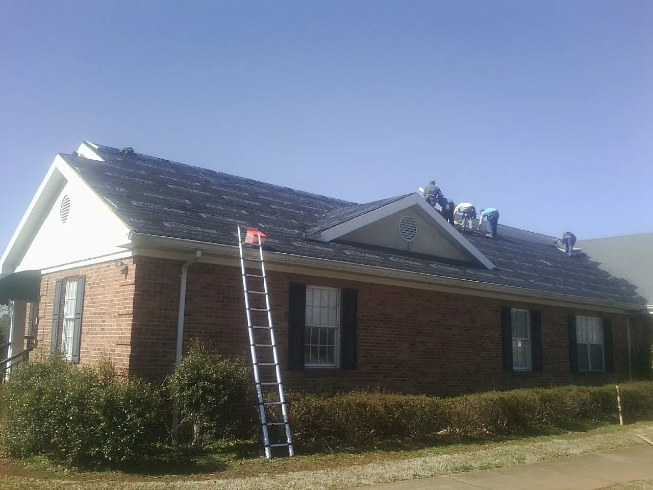 Crew tearing shingles off a brick ranch roof with a ladder set — Emergency Roof Repair work by our crew in Avoca