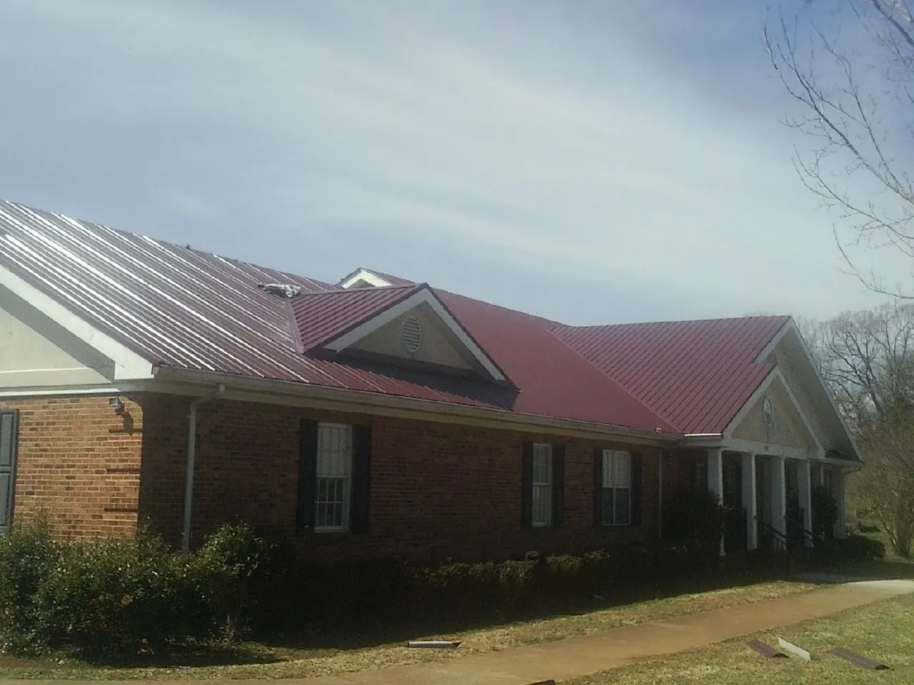 Red metal roof with gabled entries on a long brick building, from a Hail Damage Roof Repair job in Avoca