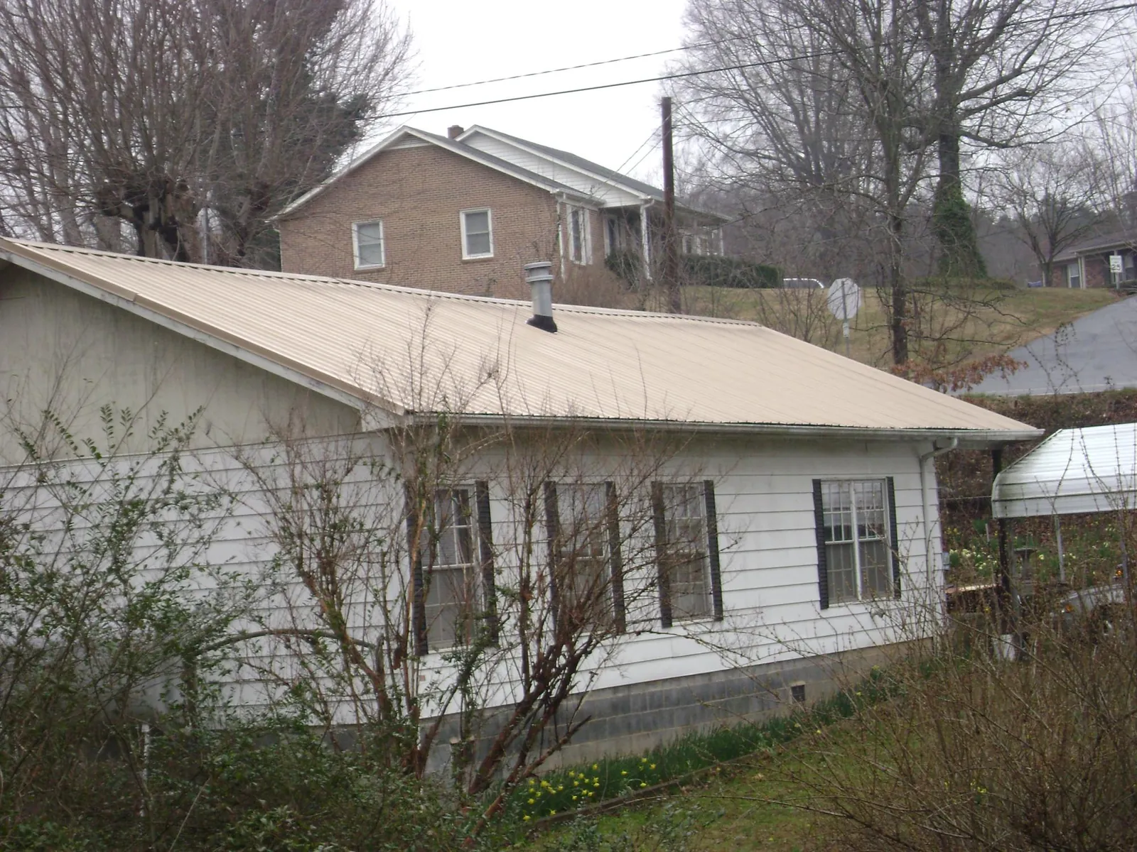 Tan metal roof on a white sided house set into a hillside — Commercial Roofing by Roofing Brothers in Avoca
